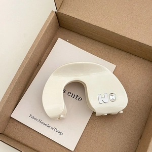 Close-up of cream acetate hair claw with silver letter H and rhinestone detailing