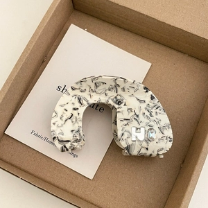 Close-up of marble pattern acetate hair claw with silver letter H and rhinestone
