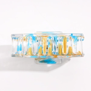 Détail d'une pince à cheveux carrée transparente avec des textures marbrées bleues et or