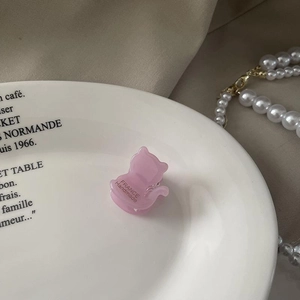 Détail d'une pince à cheveux chat en acétate rose avec lettrage doré sur une assiette