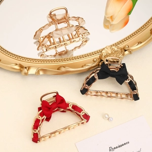 Three elegant metal bow hair claws in cream, black, and red with gold chain detailing
