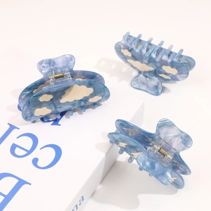 Detailed view of sky blue acetate hair claws with white cloud patterns and metal springs