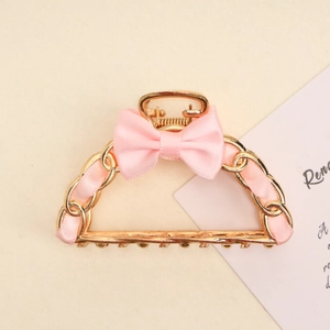 Detailed close-up of a golden hollow bow hair claw clip with pink ribbon weaving