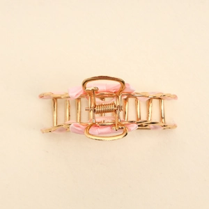Close-up of golden hollow metal hair claw with elegant pink ribbon woven decoration