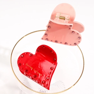 Detail von roten und rosa Herz-Haarklammern mit funkelnden Strasssteinen in Glasschale