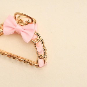 Detailed close-up of golden hollow metal hair claw with pink ribbon and bow tie
