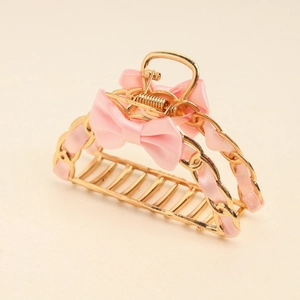 Detail of golden hollow metal shark hair claw clip with pink silk ribbon bow decoration