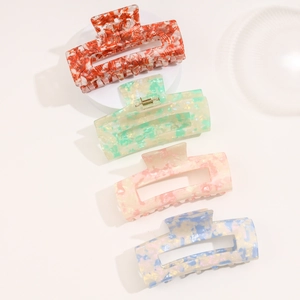 Detail of four acetate rectangle hair claws in marble colors on white pedestal display