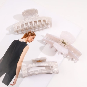 Three elegant white marble acetate hair claws with gold springs on a magazine background
