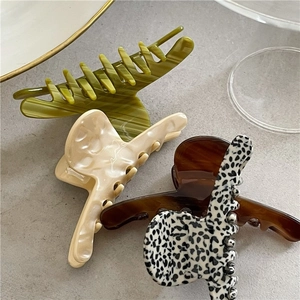 Three medium acetate hair claws in marble green, cream, and leopard patterns on stone surface