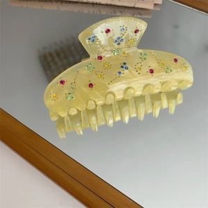 Detailed macro view of yellow resin hair claw clip with colorful rhinestone floral pattern