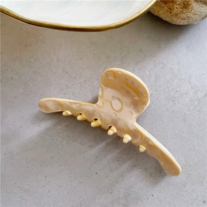Detailed view of beige acetate hair claw clip with marble texture on stone surface