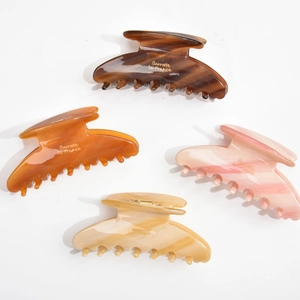 Detail view of large acetate claw clips in tortoiseshell and amber with golden logo