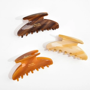 Detail view of acetate hair claws in dark coffee and amber marble textures with gold logo