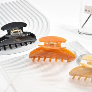 Close-up of three large acetic acid hair claw clips in black, amber, and beige colors