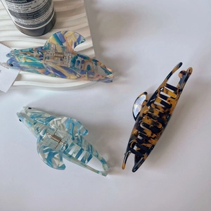 Three acetate dolphin hair claws in colorful marble and tortoiseshell patterns on a tray