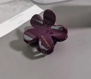 Close-up of deep purple camellia hair claw clip with glossy finish and logo detail