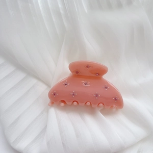 Detail of peach pink acetate hair claw clip with matching pink rhinestones on white fabric