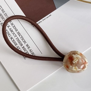 Élastique à cheveux marron avec breloque tulipe en résine marbrée sur fond de magazine