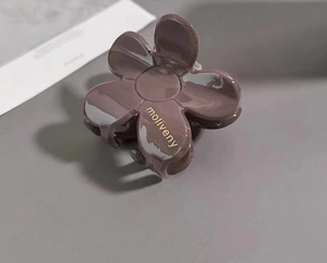 Detailed view of dark purple camellia flower hair claw clip with golden brand lettering