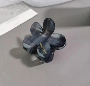 Macro detail of camellia hair claw clip with grey marble texture and gold brand logo