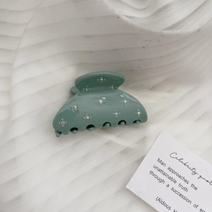 Close-up of mint green acetate hair claw clip with sparkling rhinestones on fabric