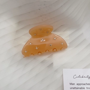 Macro shot of amber acetate hair claw clip with rhinestones on soft white fabric