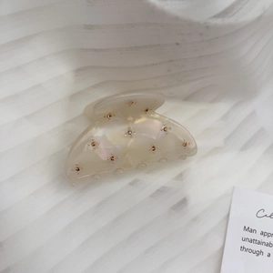 Close-up of a cream acetate hair claw clip decorated with golden rhinestone patterns