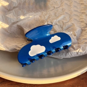 Detail of glossy navy blue acetate hair claw clip featuring white cloud patterns