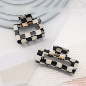 Detail view of black and white checkered acetate hair claws with gold logo engraving