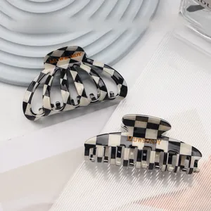 Close-up of black and white checkered acetate hair claws with gold logo on a textured plate