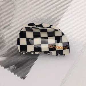 Detail view of a black and white checkered acetate hair claw clip with gold brand lettering