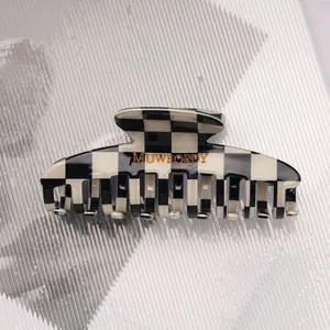Detail of checkered hair claw clip with black and white pattern and gold brand logo