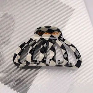 Detailed macro view of black and white checkered acetate hair claw clip with golden logo