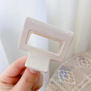 Close-up of a cream rectangular hair claw clip held by hand in a cozy home setting