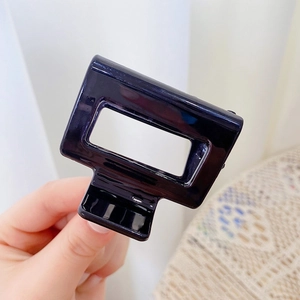 Detail shot of a black glossy resin shark hair claw clip held by hand showing square design
