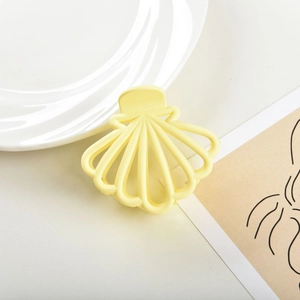Detail shot of a matte yellow shell hair claw clip styled on a white ceramic plate