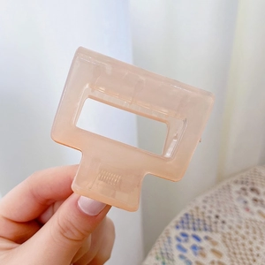 Close-up of peach pink rectangular hair claw clip with smooth resin texture and metal spring