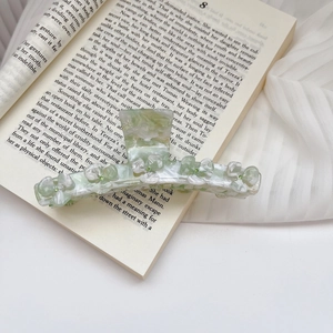 Detail of large acetate hair claw clip with floral marble texture and green rhinestones