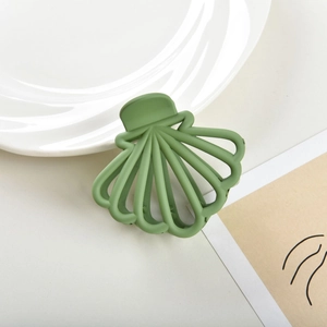 Detail view of a shell-shaped matte sage green hair claw clip on a ceramic plate