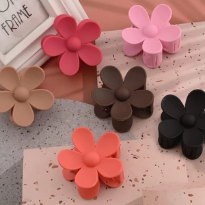 Detail showing various colors of matte flower hair claws arranged on a stone surface