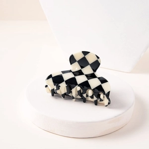 Detail of checkered hair claw clip on a minimalist white stand showing retro fashion design