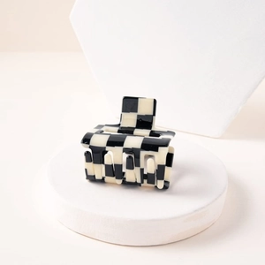 Retro black and white checkerboard hair claw clip displayed on a minimalist pedestal