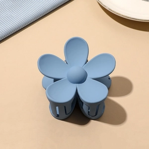 Detailed close-up of a matte light blue flower hair claw clip on a soft textured background