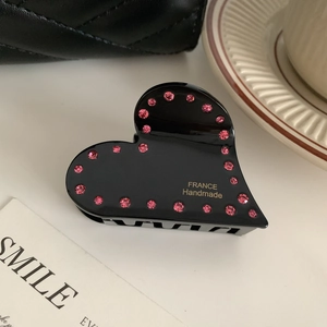 Dettaglio di un mollettone a cuore nero con strass rosa e scritte dorate fatte a mano