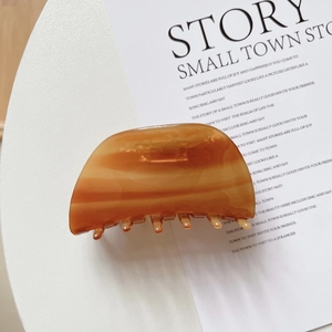 Detailed close-up of shell-shaped acetate hair claw clip with amber tortoiseshell texture