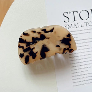 Detailed view of tortoiseshell acetate hair claw clip with leopard pattern on white plate