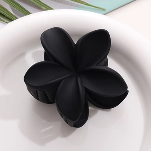 Détail d'une pince à cheveux fleur de frangipanier noir mat sur une assiette en céramique