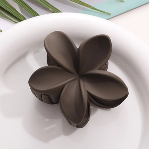 Détail d'une pince à cheveux fleur de frangipanier marron foncé mat sur une assiette