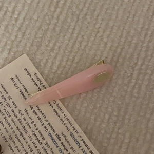 Detail of leaf-shaped light pink resin hair clip with gold metal accent on beige fabric